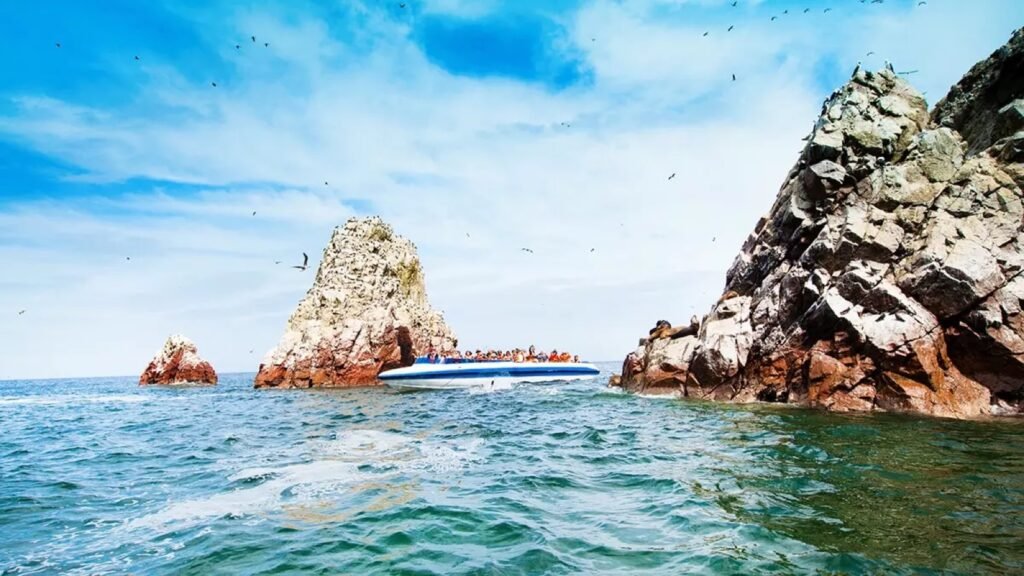 Bote turístico junto a las rocas de las islas Ballestas, cubiertas de aves marinas, en Paracas