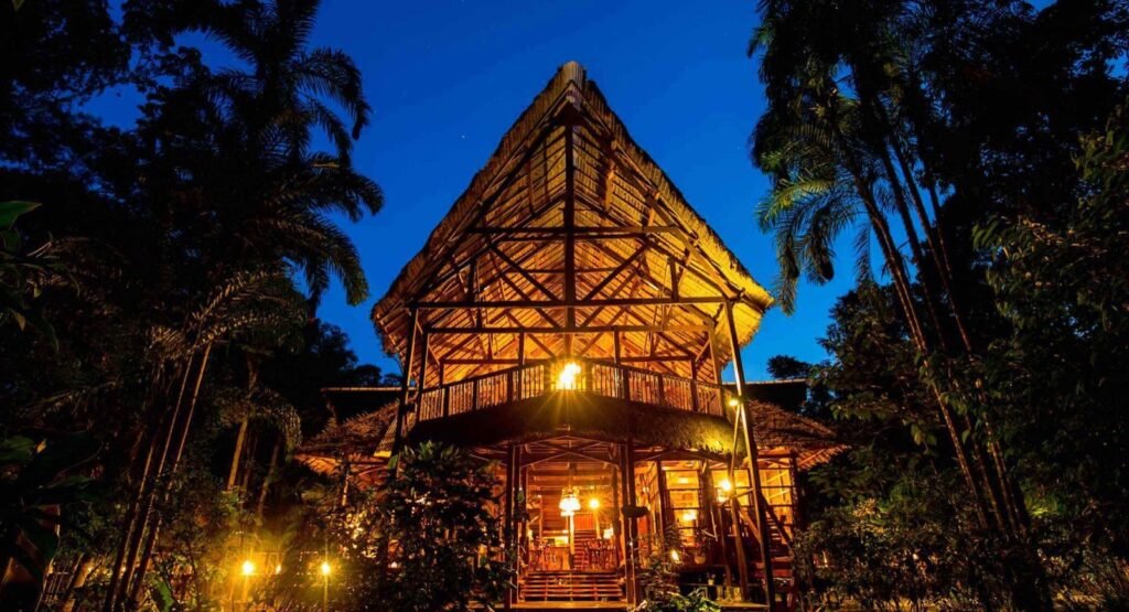 Lodge de madera con techo de palma iluminado de noche entre la selva de Tambopata